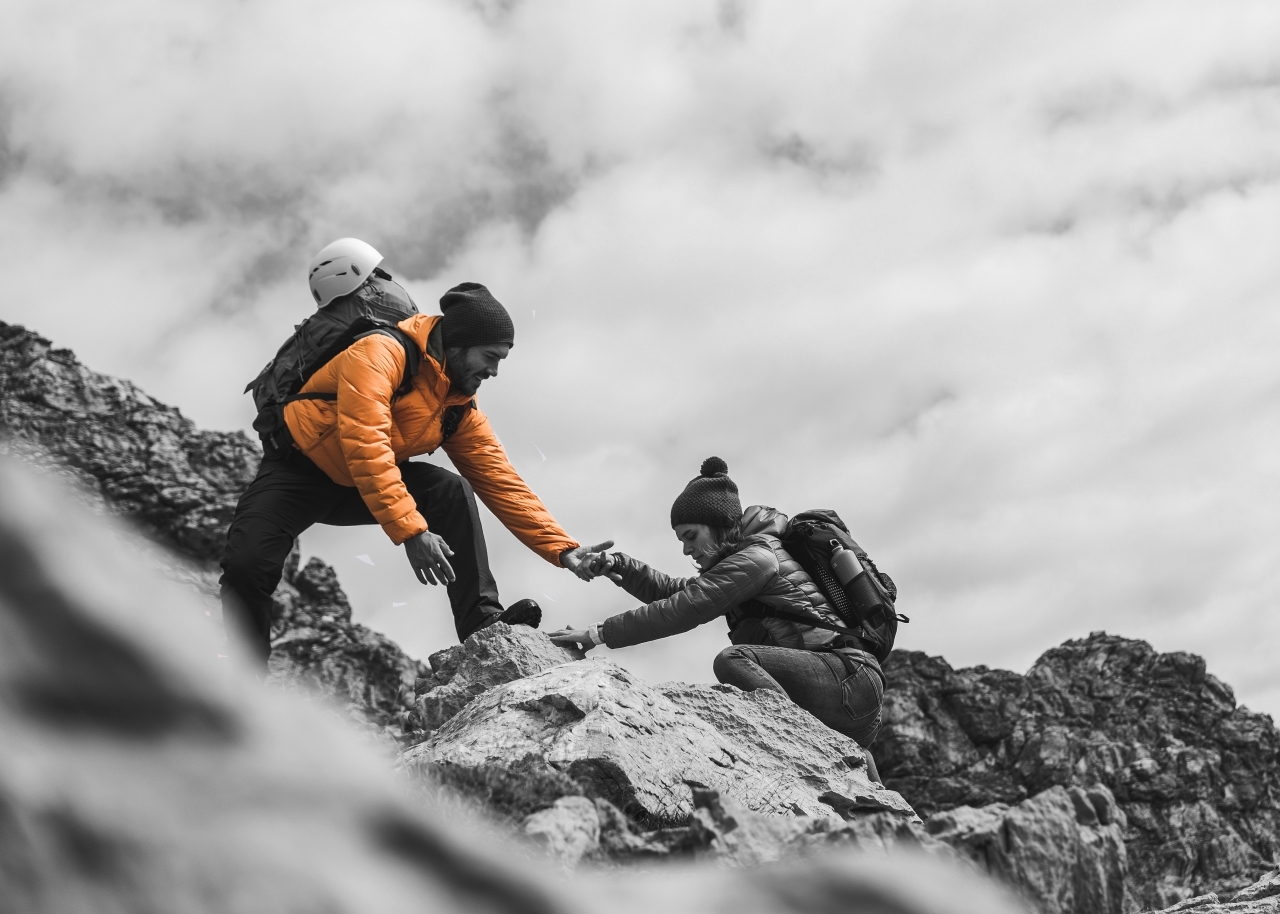 Climber helping another climber to the top of a rock slope